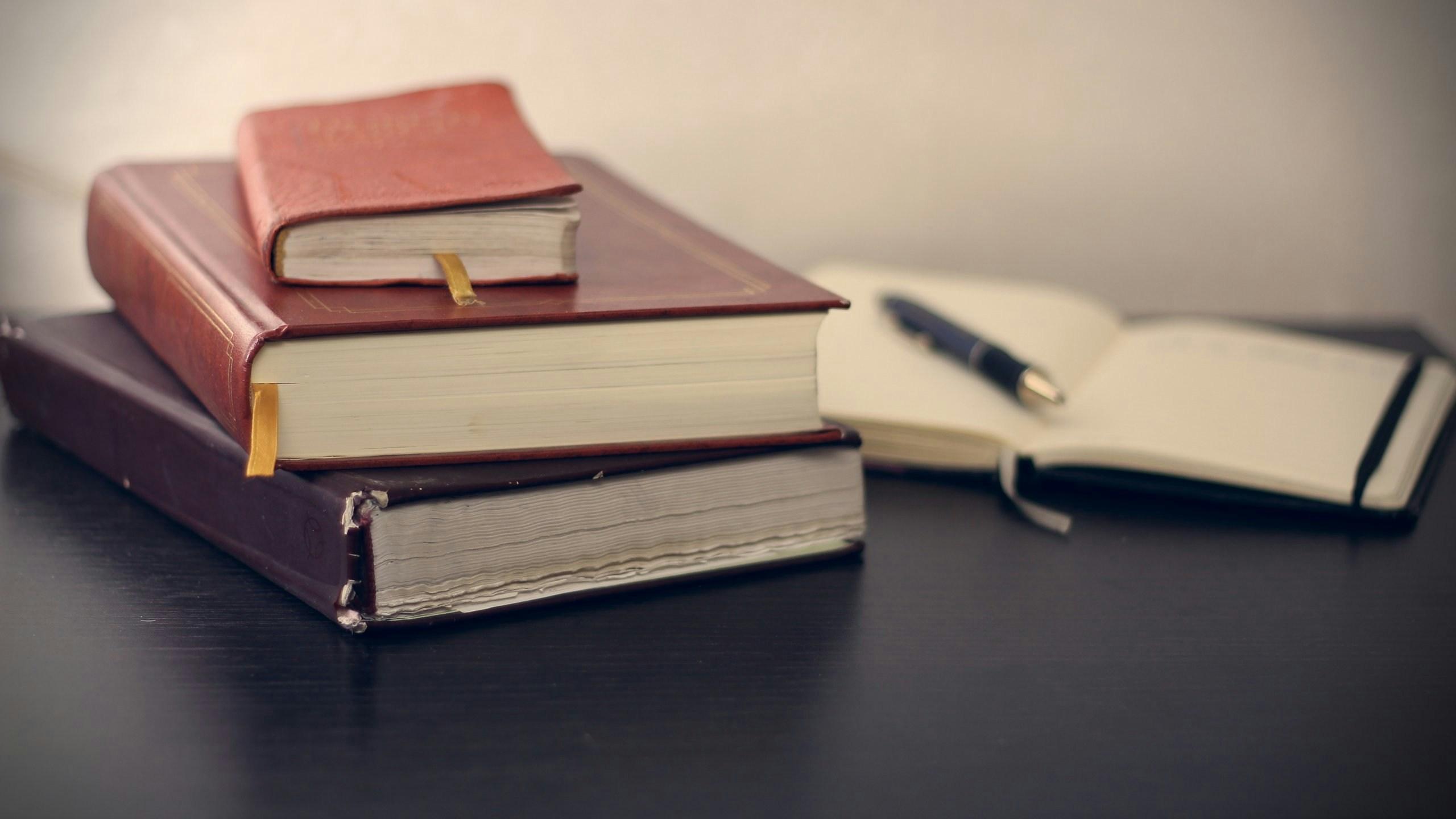 A stack of three leather-bound books on a table, with an open journal and pen lying next to them.