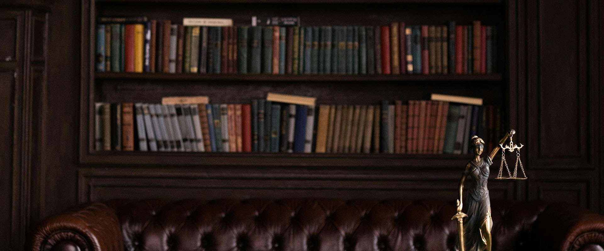 A statue of Lady Justice on a desk in an office. There is a bookshelf with a library of books along the wall.